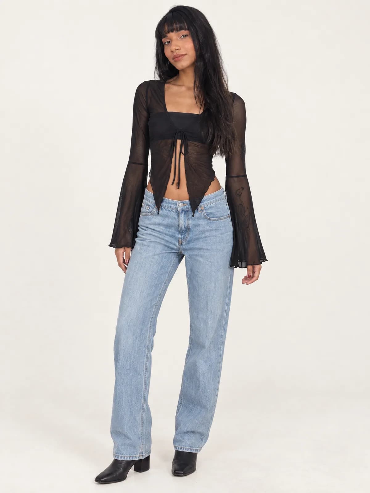 Adriely de frente com blusa de tule preta com amarração e mangas sino, jeans claro