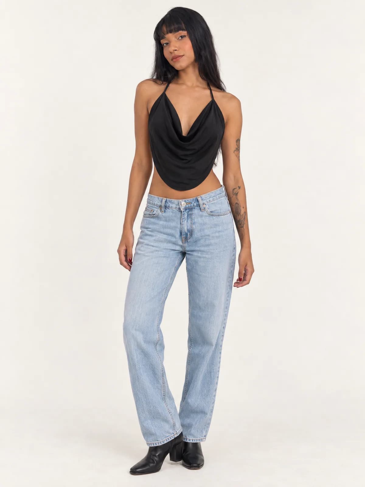 Modelo de frente com top frente única preto de decote degagê e barra arredondada, calça jeans clara